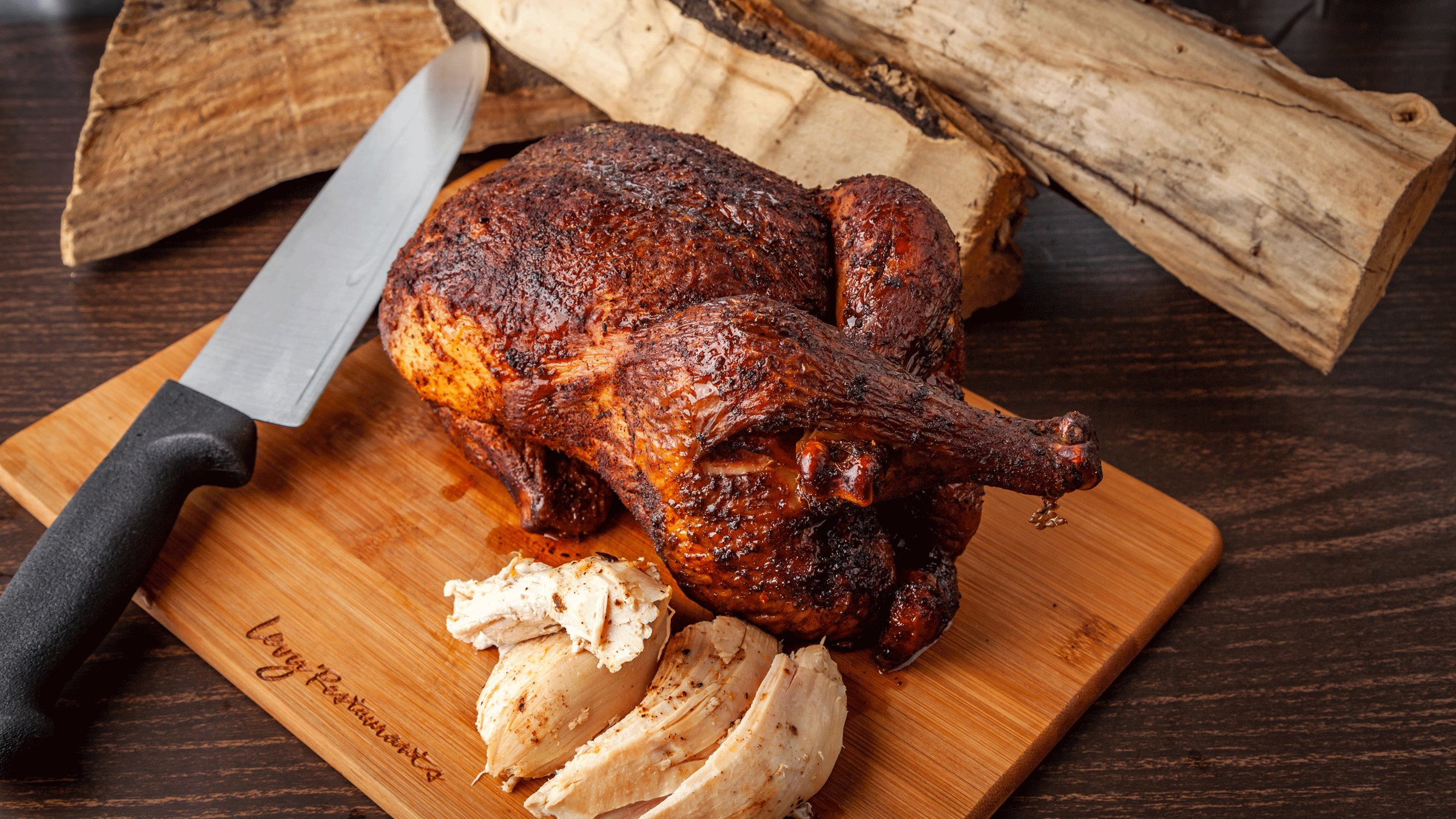 A whole baked chicken on a wood carving board with a knife next to it